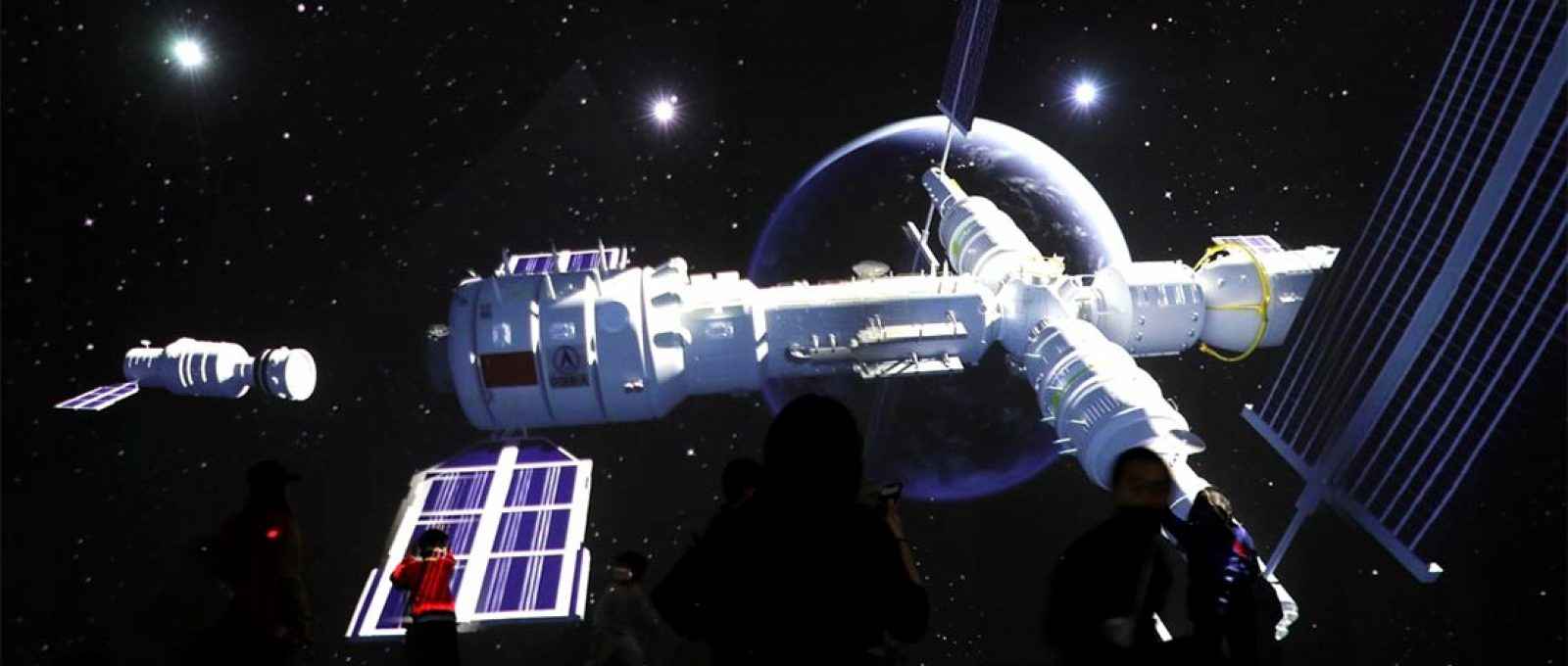 Visitantes perto de tela gigante com imagens da estação espacial Tianhe em exposição que mostra o desenvolvimento da exploração espacial chinesa no Museu de Ciência e Tecnologia da China em Pequim (Foto: Tingshu Wang/Reuters).