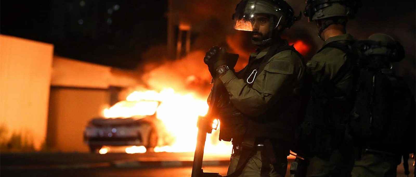 Membros da força de segurança israelense perto de um carro da polícia em chamas durante confrontos entre a polícia israelense e membros da minoria árabe na cidade árabe-judaica de Lod, Israel, 12 de maio de 2021 (Foto: Ammar Awad/Reuters).