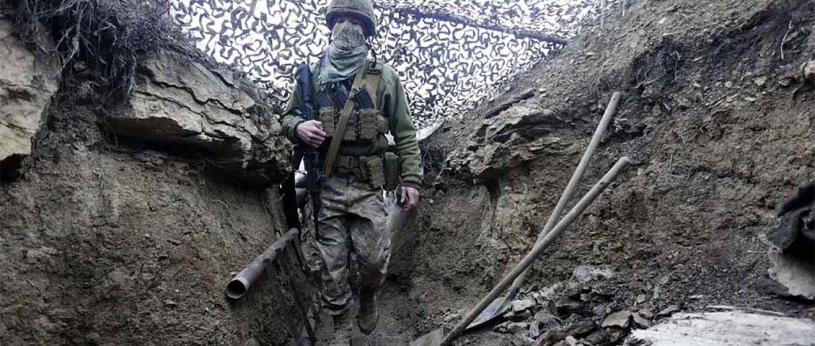 Soldado ucraniano caminha sob rede de camuflagem em uma trincheira na linha de separação de rebeldes pró-Rússia na região de Donetsk, na Ucrânia, em 3 de dezembro (Andriy Dubchak/AP).