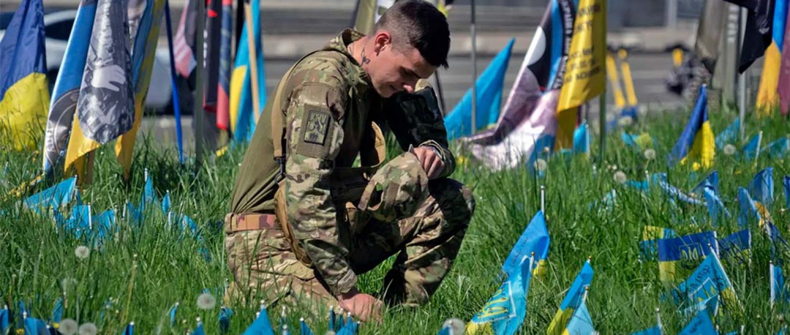Soldado ajoelhado na Praça da Independência em Kiev, quarta-feira, 1º de maio de 2024, cercado por bandeiras que simbolizam os soldados ucranianos mortos na guerra com a Rússia (Efrem Lukatsky/AP).
