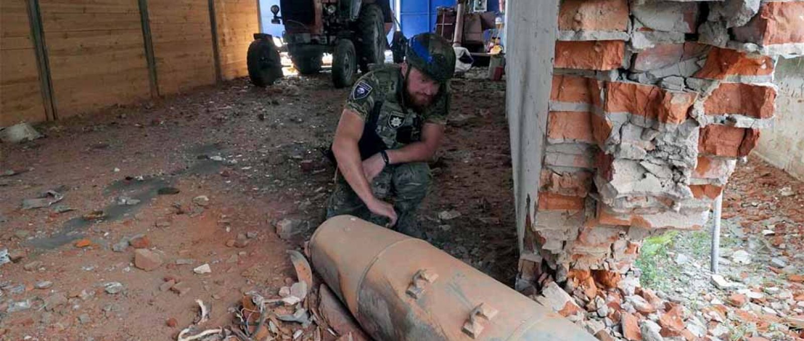 Policial inspeciona uma bomba não detonada de 250 kg após ataque aéreo russo no armazém agrícola de Bilyi Kolodiaz, região de Kharkov, Ucrânia, 11 de julho de 2024 (Andrii Marienko/Associates Press).